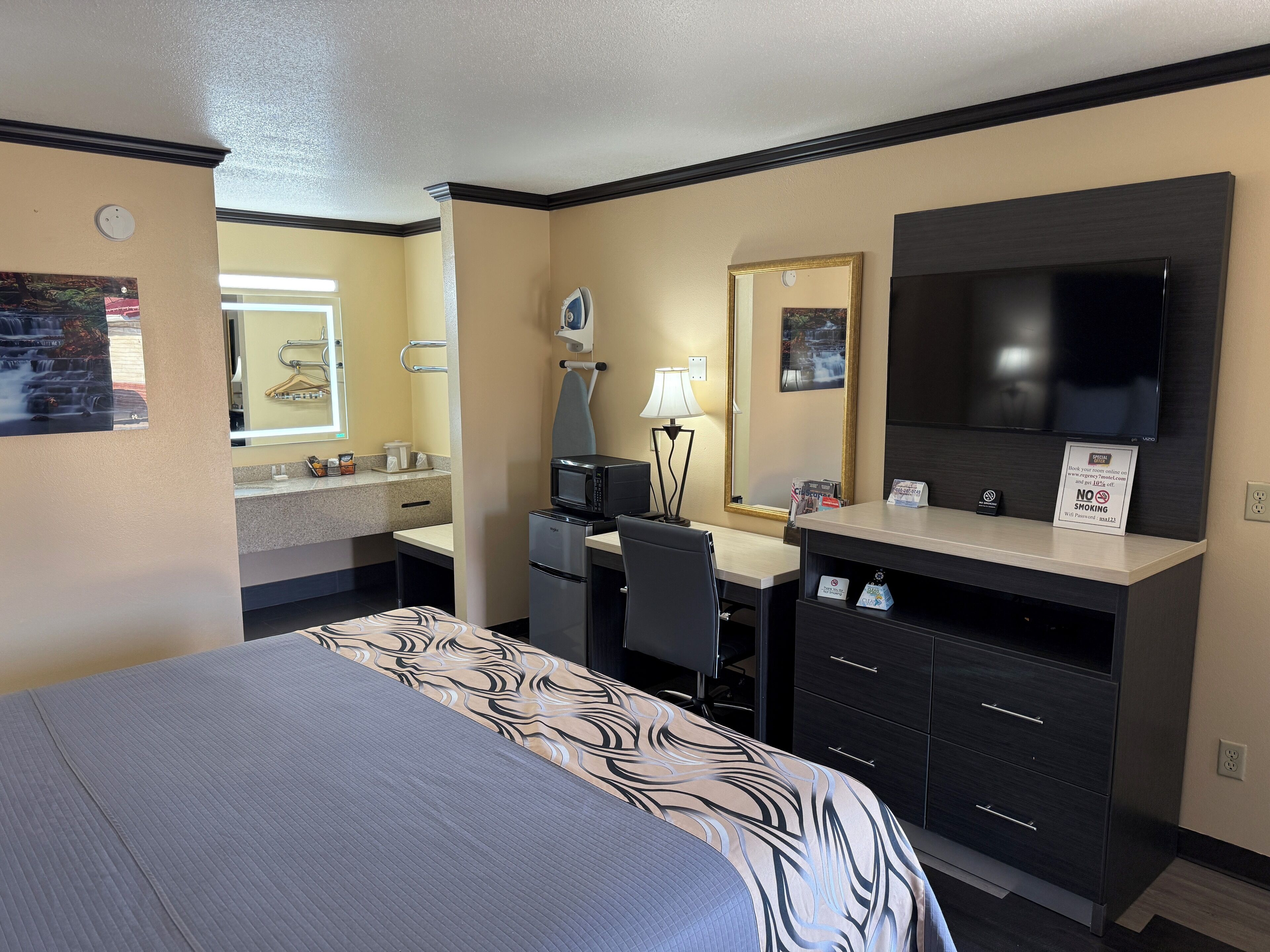 Een hotelkamer met een bed, een bureau met een computer, een televisie, een spiegel en een kleine kitchenette.