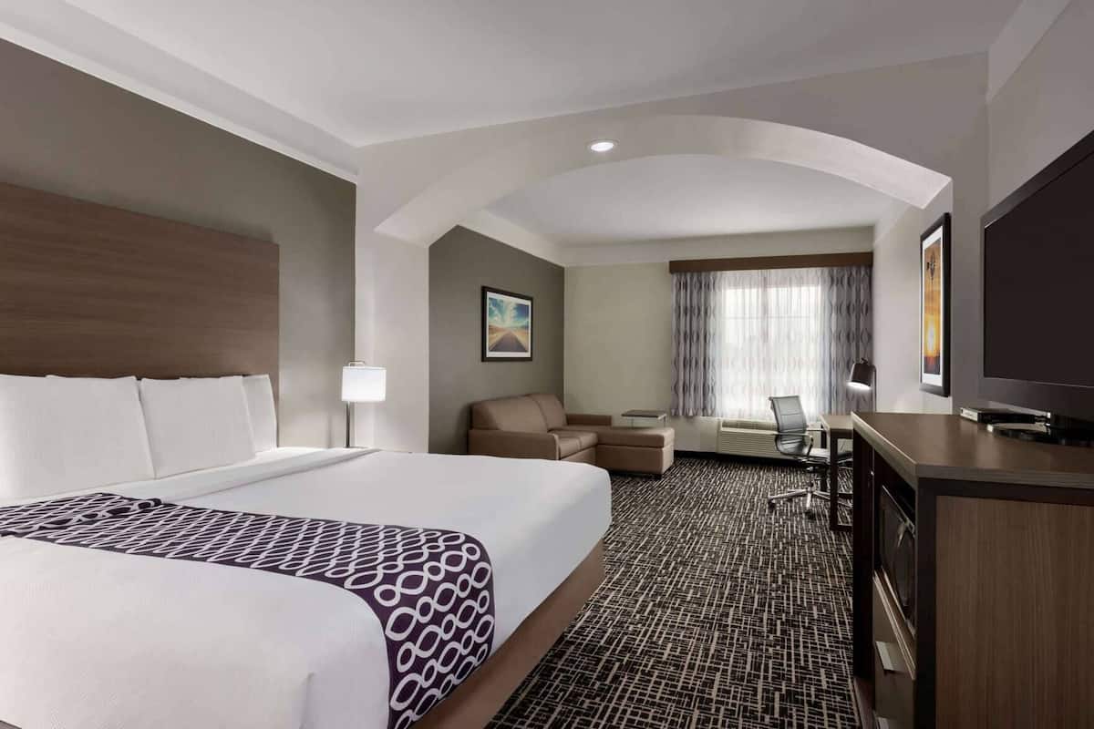 A hotel room with a large bed, a desk, a chair, a television, and a window with curtains.