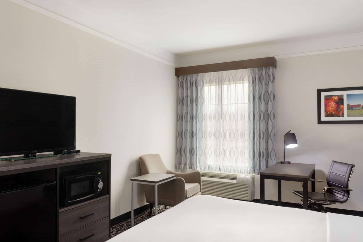 A hotel room with a bed, a TV, a desk, a chair, a lamp, and a window with curtains.