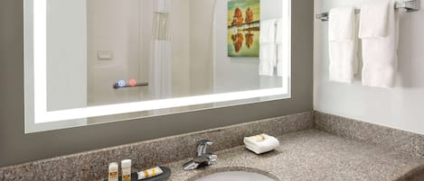 Une salle de bain avec un comptoir en granit, un lavabo blanc et un grand miroir. Deux serviettes sont suspendues sur un porte-serviettes et un tableau est accroché au mur.