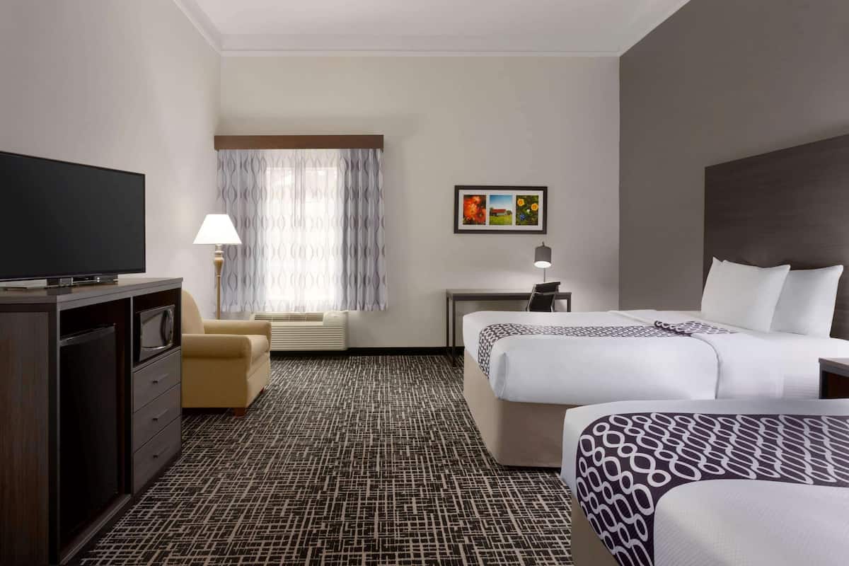 A hotel room with a large bed, a smaller bed, a desk, a television, a sofa, and a patterned carpet.