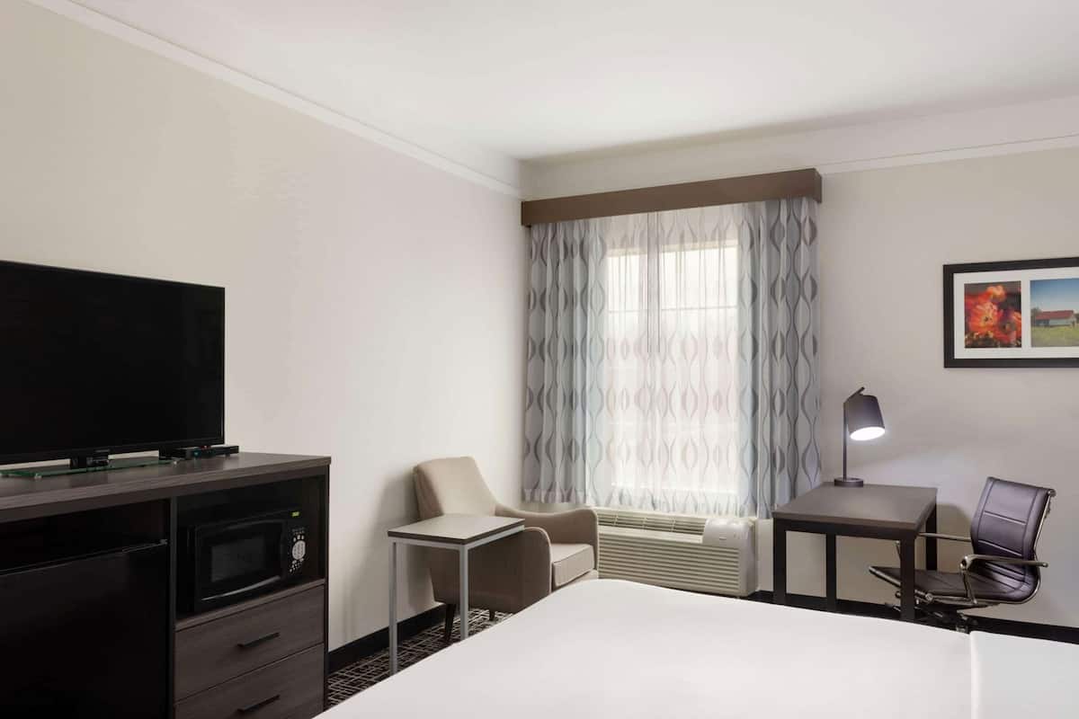 A hotel room with a bed, a TV, a desk, a chair, a lamp, and a window with curtains.