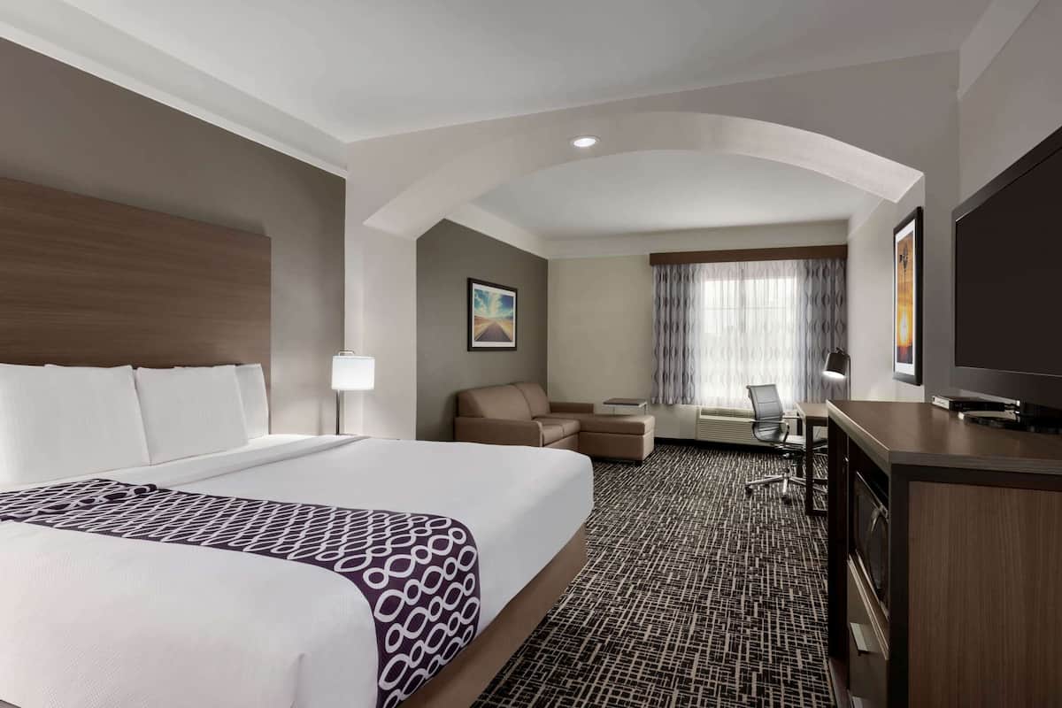 A hotel room with a large bed, a desk, a chair, a television, and a window with curtains.