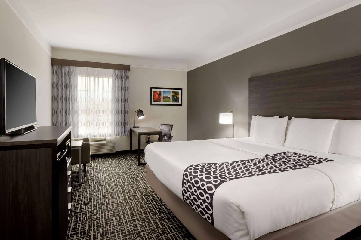 A hotel room with a large bed, a desk, a chair, a TV, and a window with curtains.