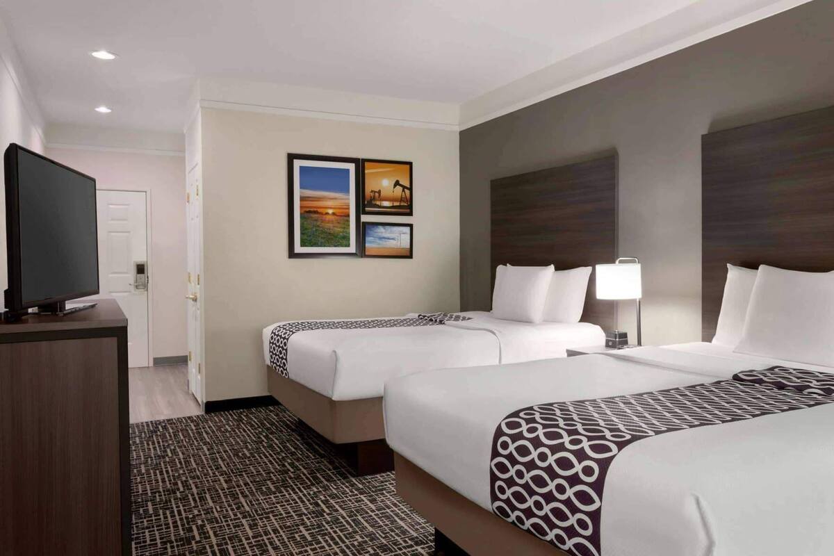 A hotel room with two beds, a TV, a desk, and artwork on the wall.