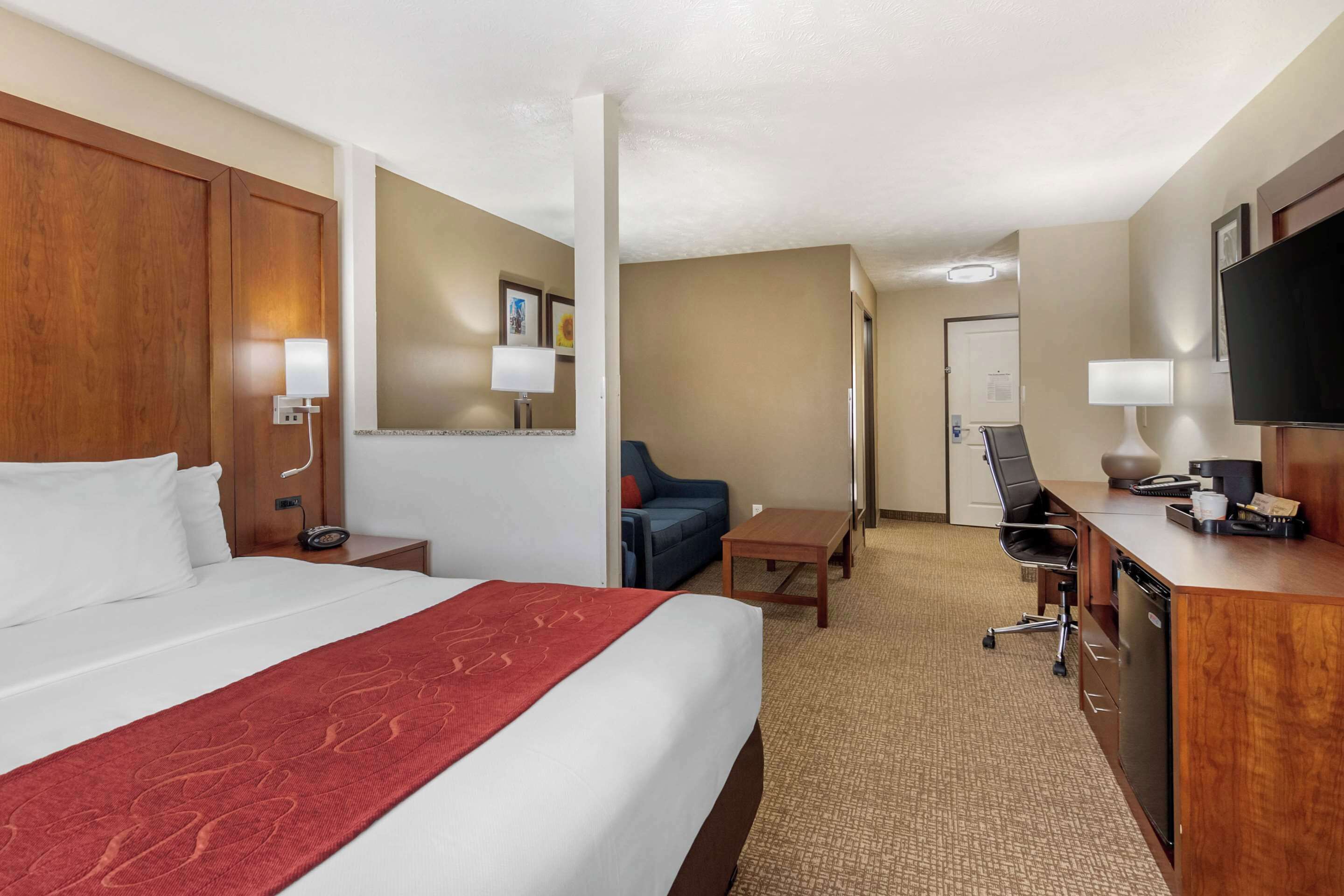 Una habitación de hotel con una cama grande, un escritorio, una silla, un televisor y una mesita.