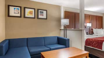 A hotel room with a blue sofa, a wooden table, and a bed with a red blanket. There are three framed pictures on the wall.