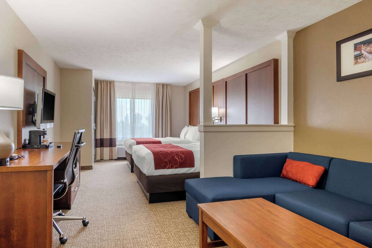Een hotelkamer met een bed, een bureau met een computer, een televisie, een bank en een raam met gordijnen.