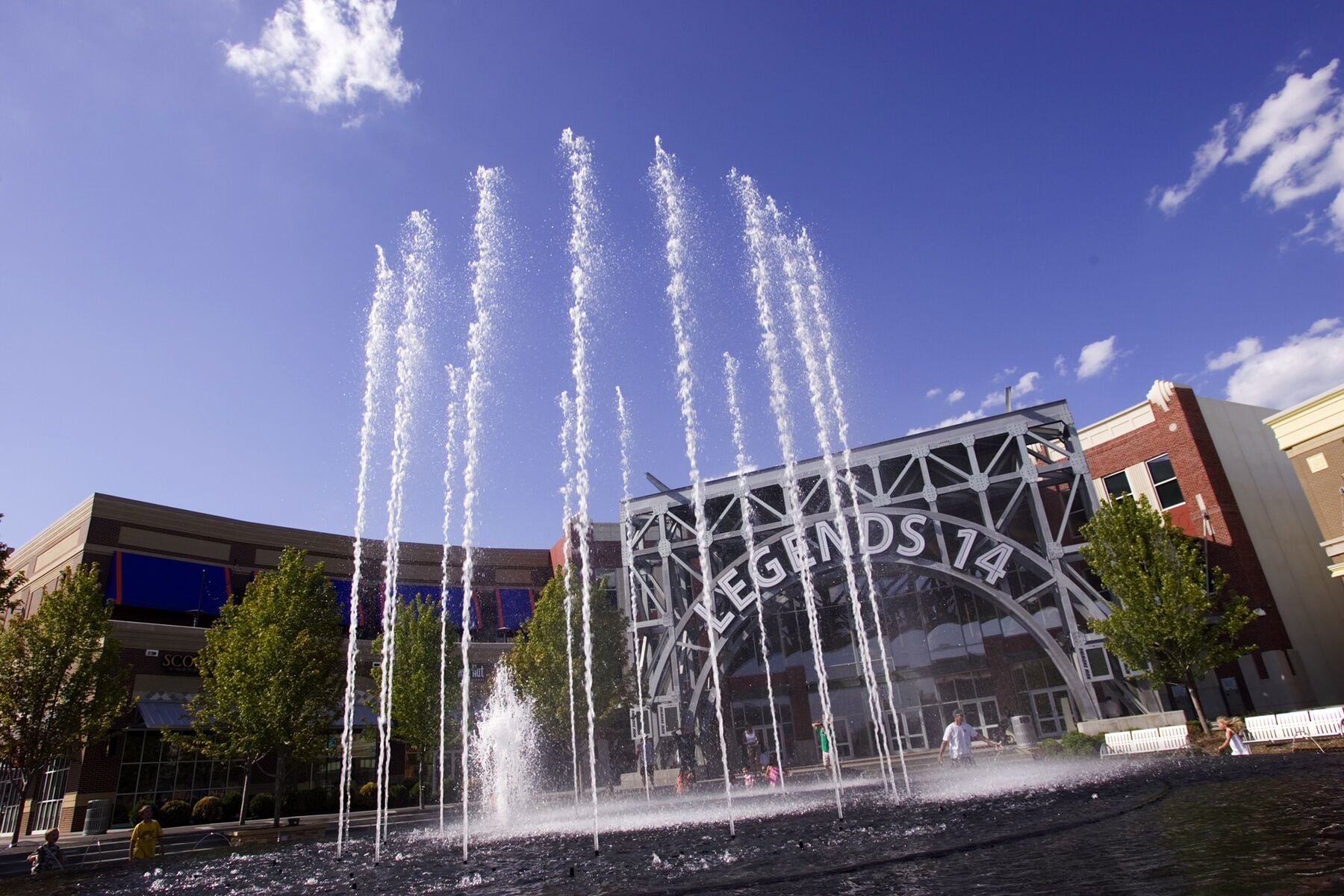 A fountain with multiple water jets in front of a building labeled "LEGENDS 14".