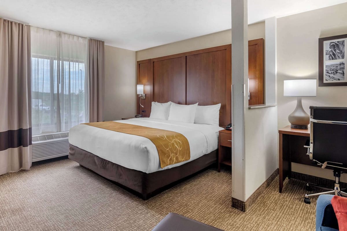 Een hotelkamer met een groot bed, een bureau, een stoel, een lamp en een raam met gordijnen.