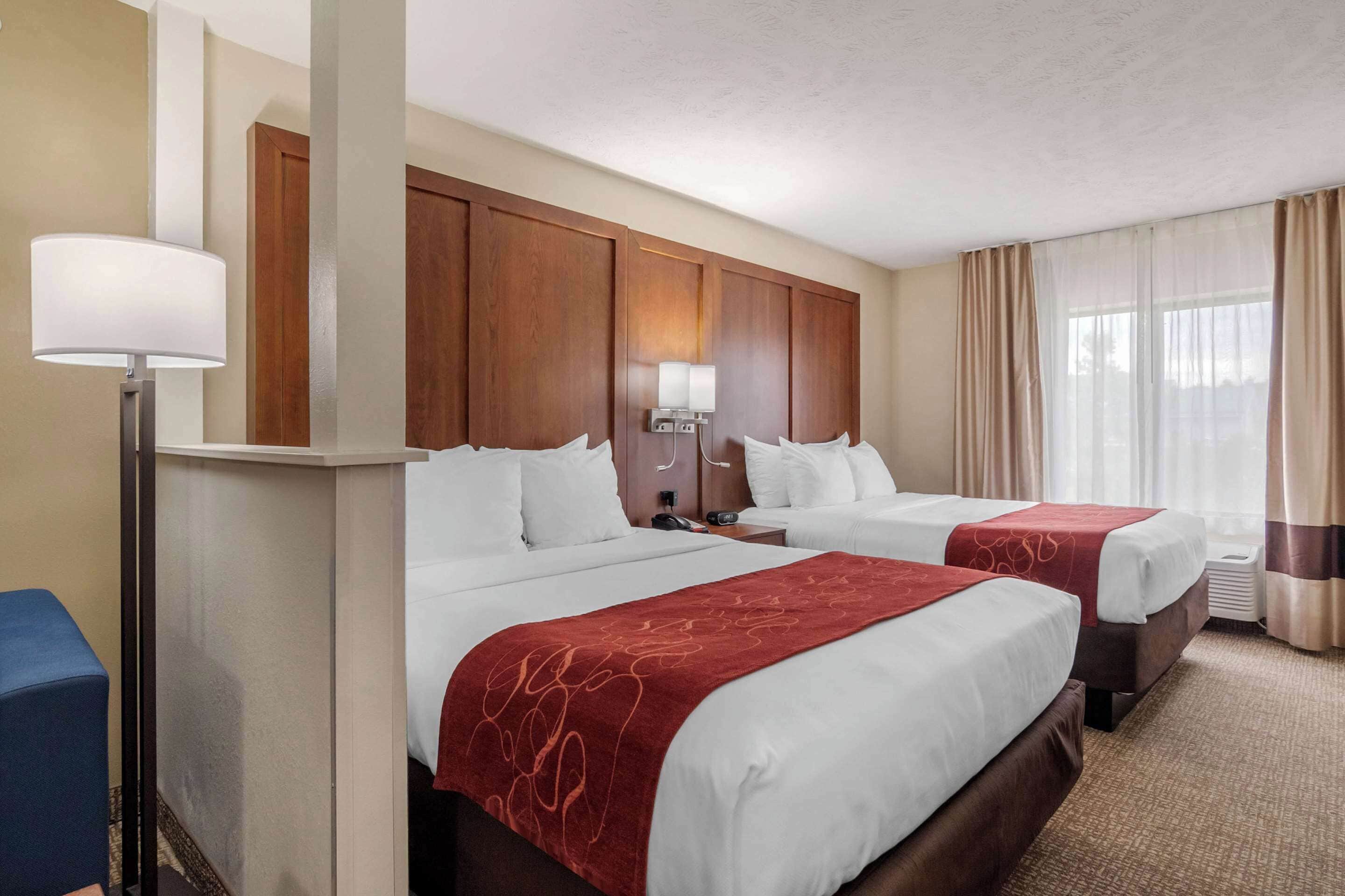 A hotel room with two beds, wooden headboards, a desk, and a lamp.