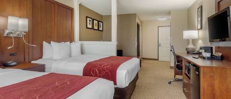 A hotel room with two beds, a desk with a television, and a bathroom visible in the background.