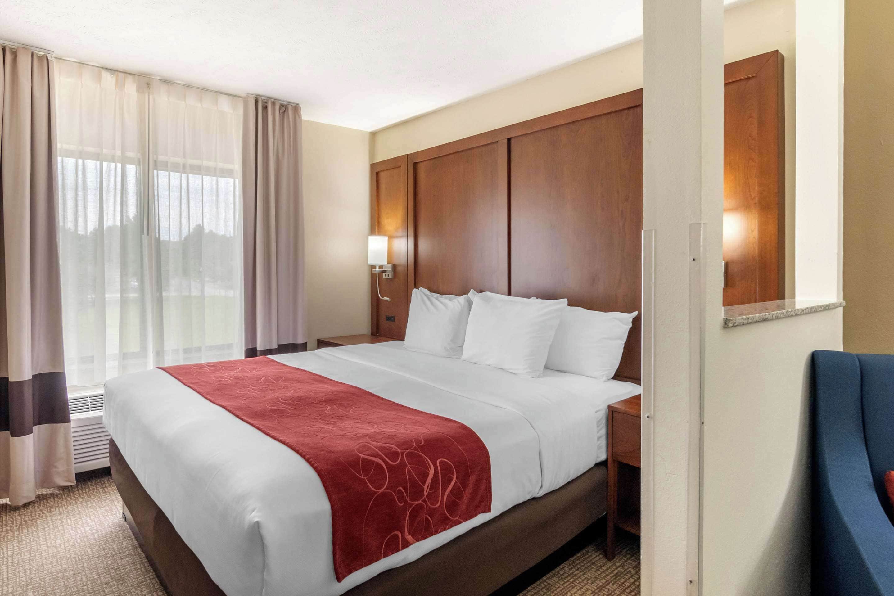 A hotel room with a large bed, a wooden headboard, a desk, and a chair.