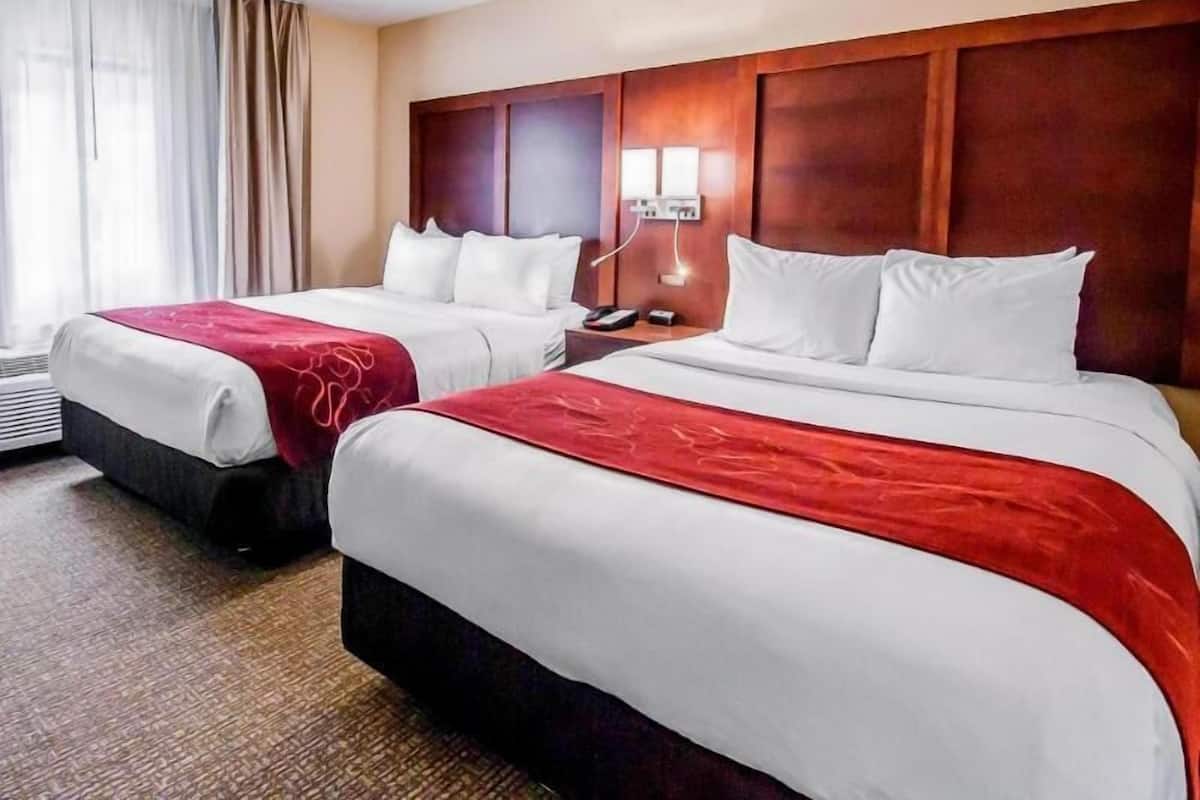 Een hotelkamer met twee bedden, een houten hoofdeinde, een nachtkastje en een raam met gordijnen.