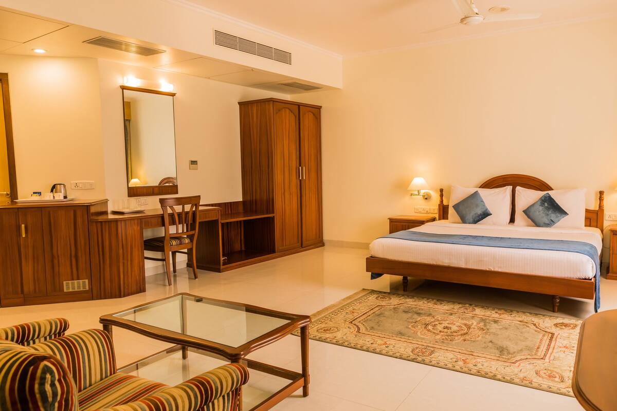 A hotel room with a bed, a desk, a chair, a sofa, and a mirror.