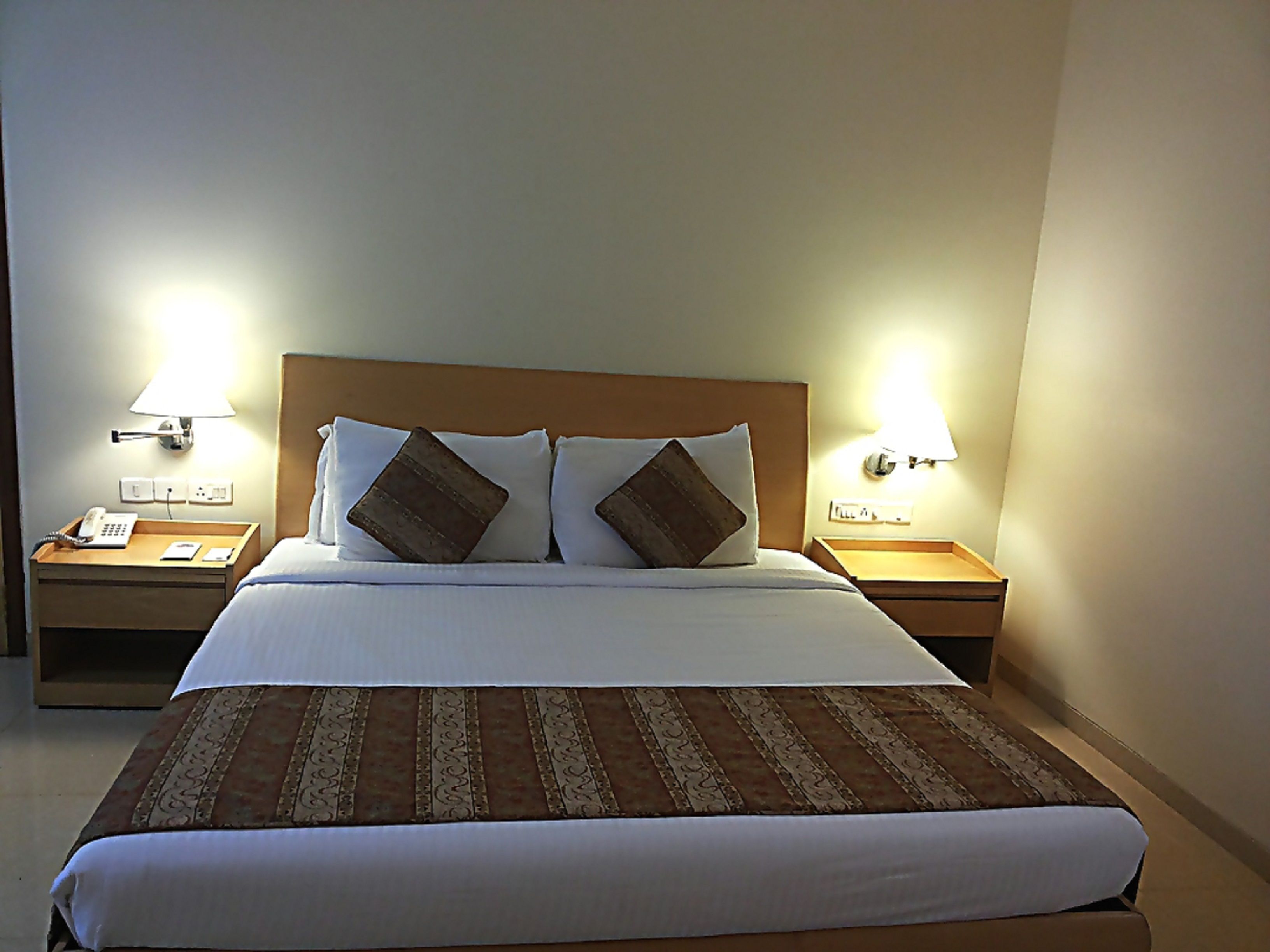 A hotel room with a large bed, two bedside tables, a nightstand with a lamp, and a telephone.