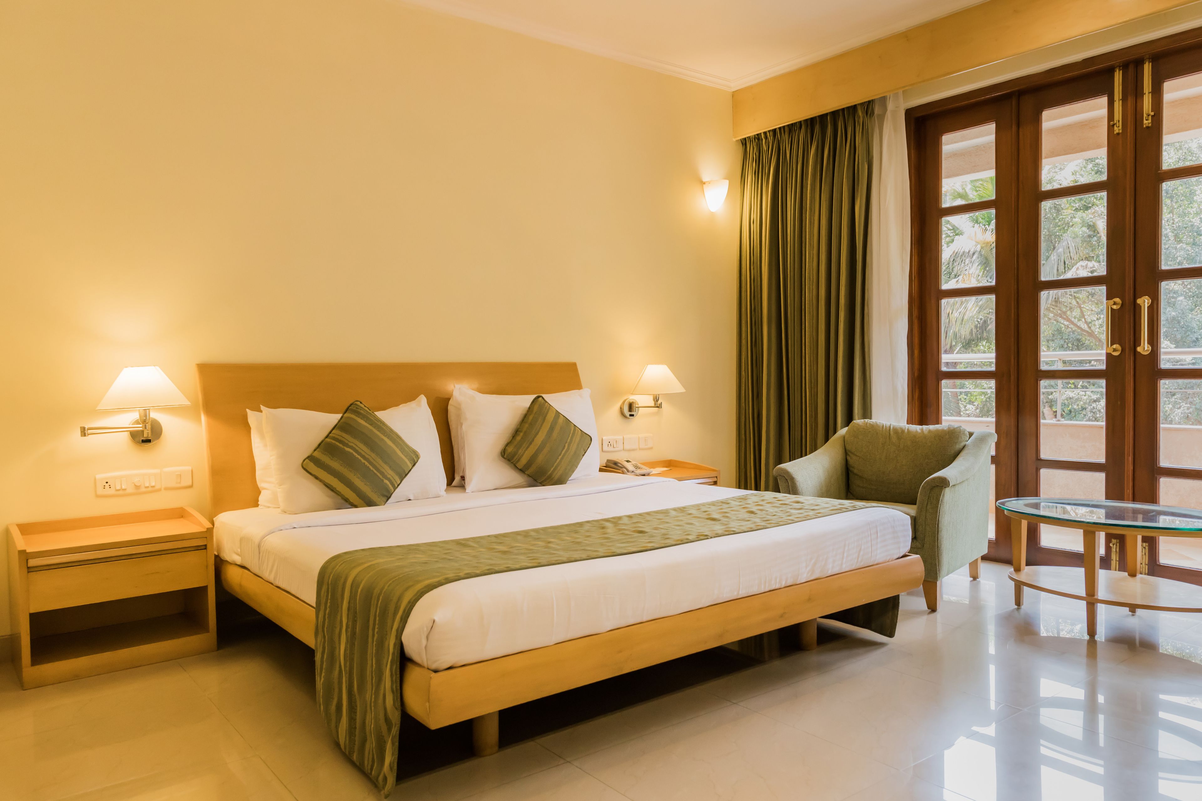 A hotel room with a large bed, two bedside tables, a chair, and a glass table.