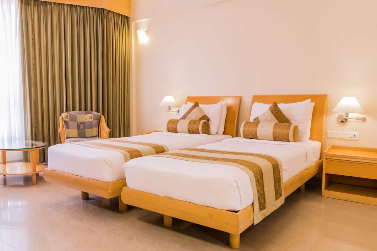 A hotel room with two beds, a small table, a chair, and a lamp.