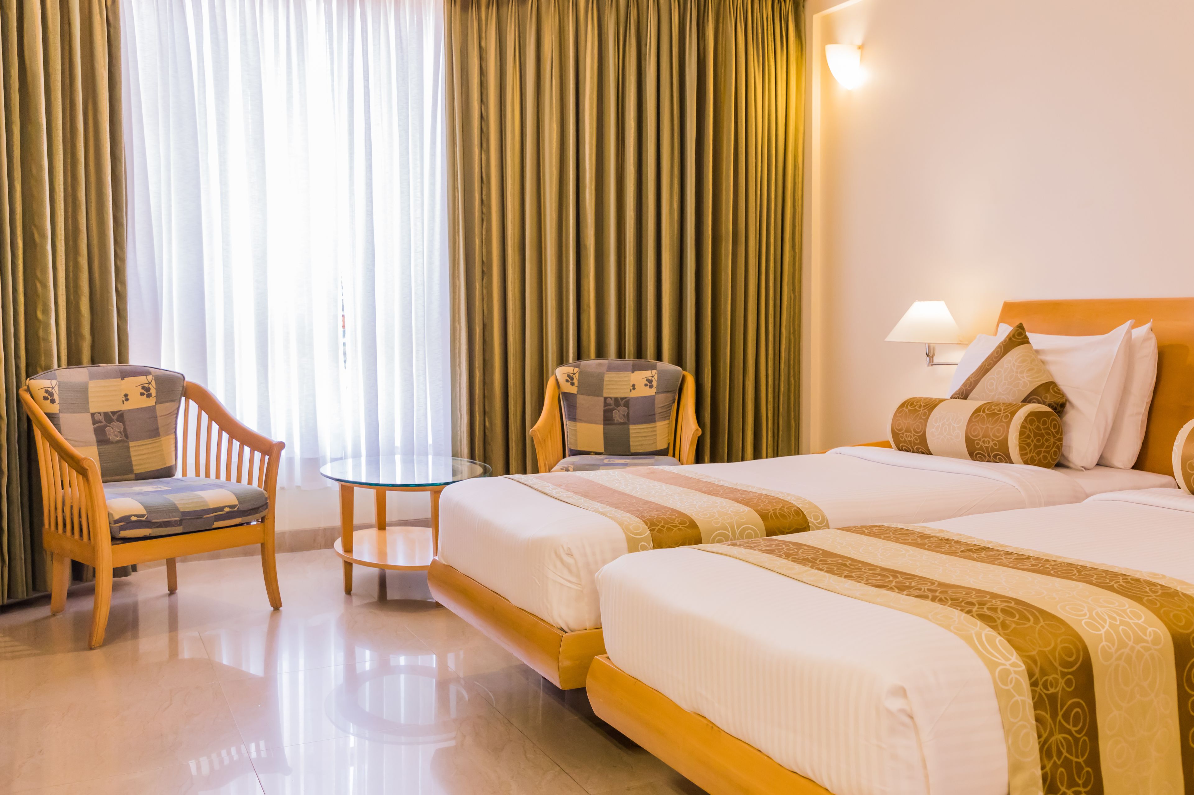 Una habitación de hotel con dos camas, una silla de madera, una mesita y una lámpara.
