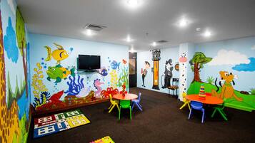 Children can play and interact in this vibrant playroom with cartoon-themed murals, colorful furniture, and a mounted TV.