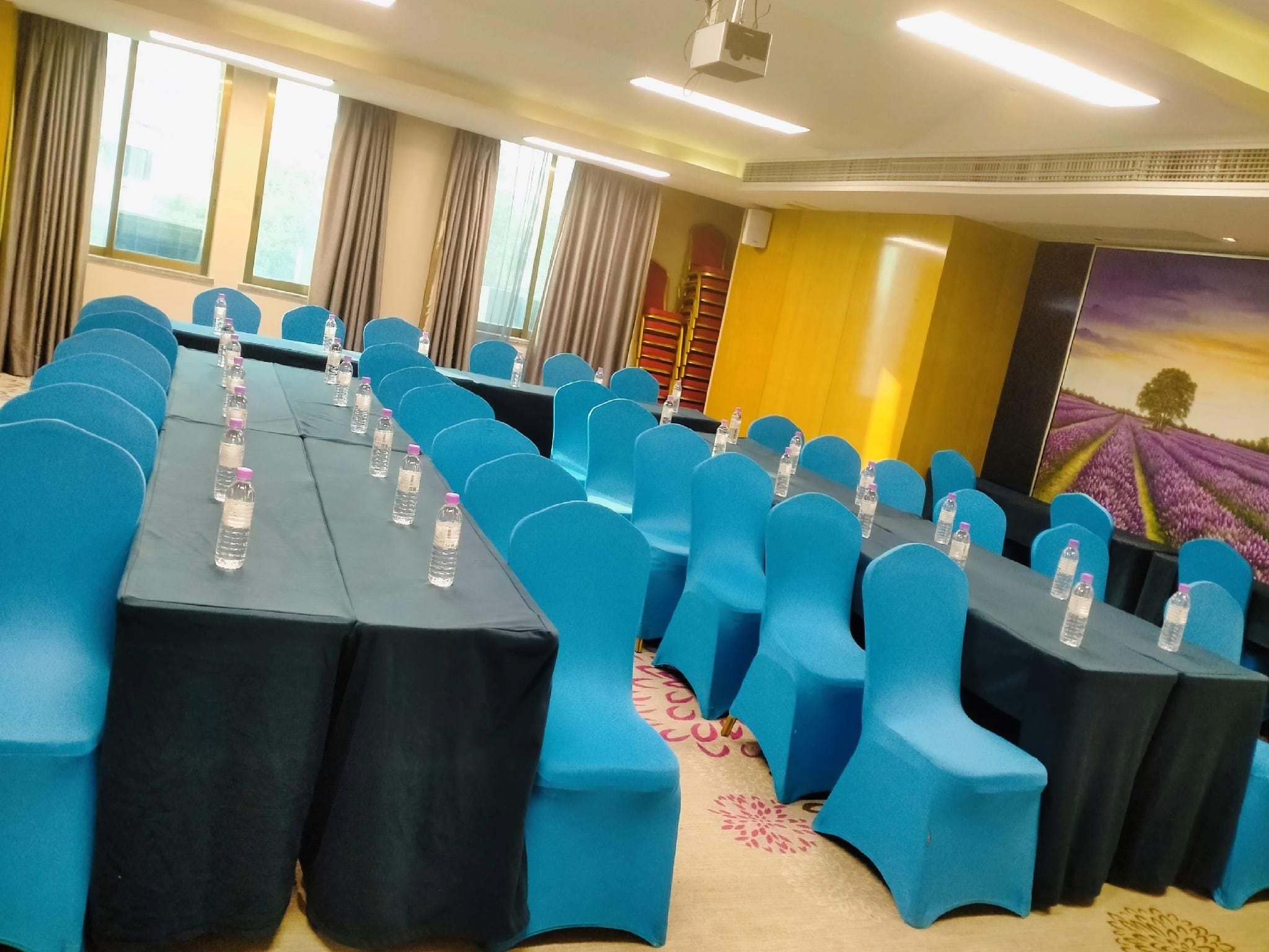 A conference room with rows of tables and chairs, water bottles on each table, and a large window with curtains.