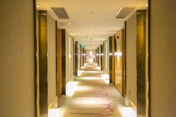 Un pasillo de hotel de diseño largo y estrecho, con varias puertas y suelo cubierto de alfombra.