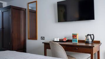 A hotel room with a bed, a desk with a chair, a television, a wardrobe, and a mirror.