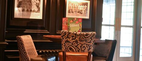 A bar area with framed photographs on the wall, a patterned chair, and a table with a drink advertisement.