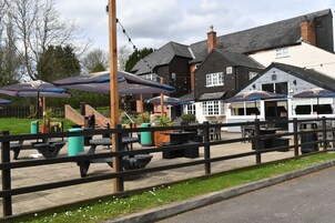 An outdoor seating area with tables and umbrellas, a wooden fence, and a building with a sloped roof in the background.