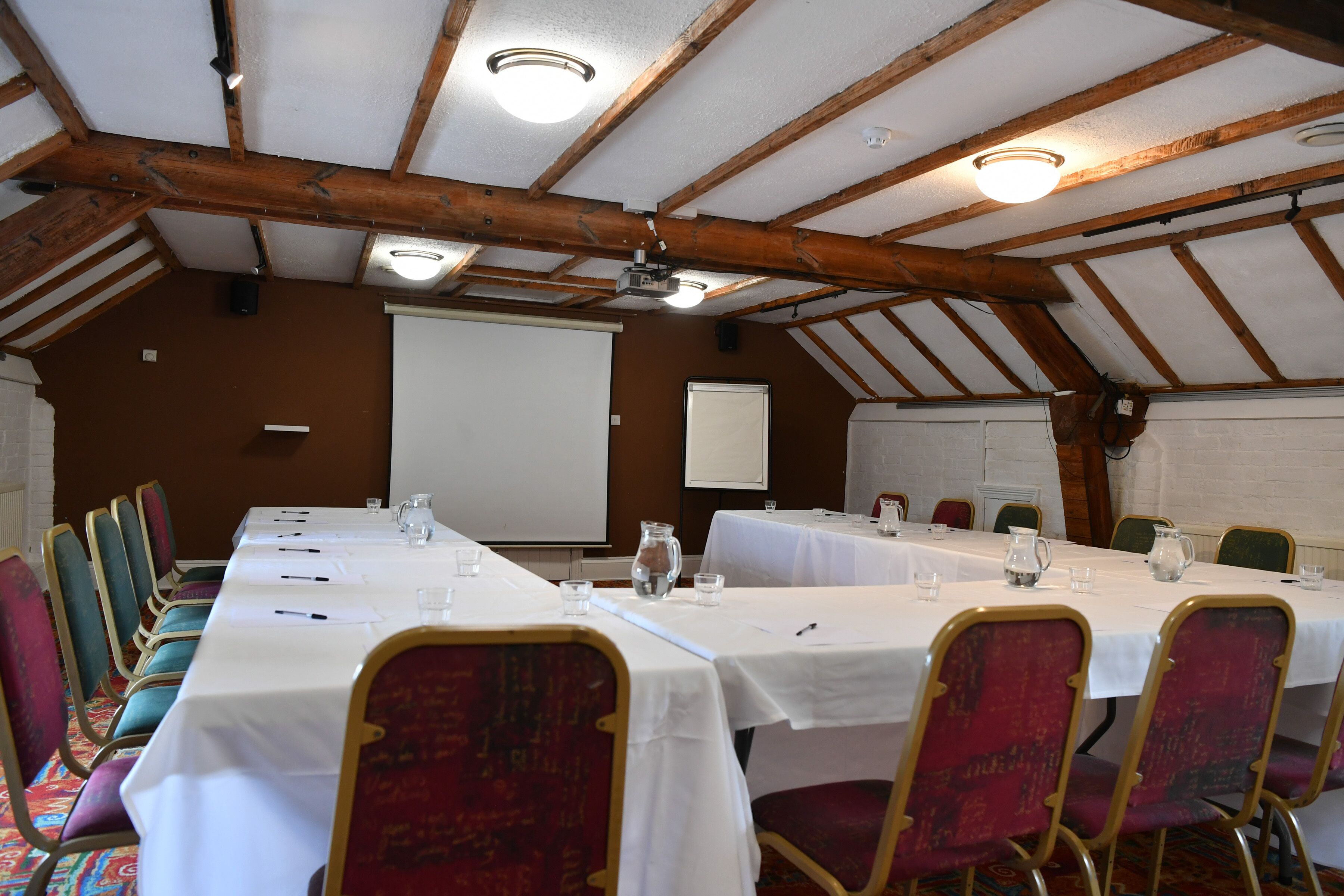 Un salón de conferencias con una larga mesa, sillas y una pantalla para proyector.