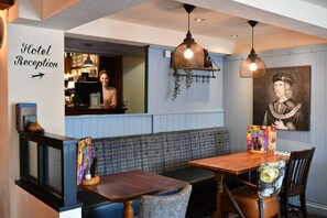A hotel reception area with a wooden reception desk, a bench, and a dining table with chairs. There is a framed picture on the wall and a sign indicating the reception area. - Mill on the Soar by Greene King Inns (Leicester)