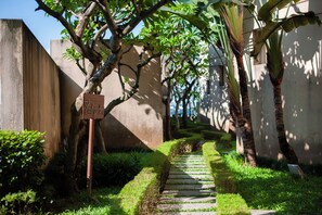 A narrow stone pathway flanked by lush greenery and a concrete wall.