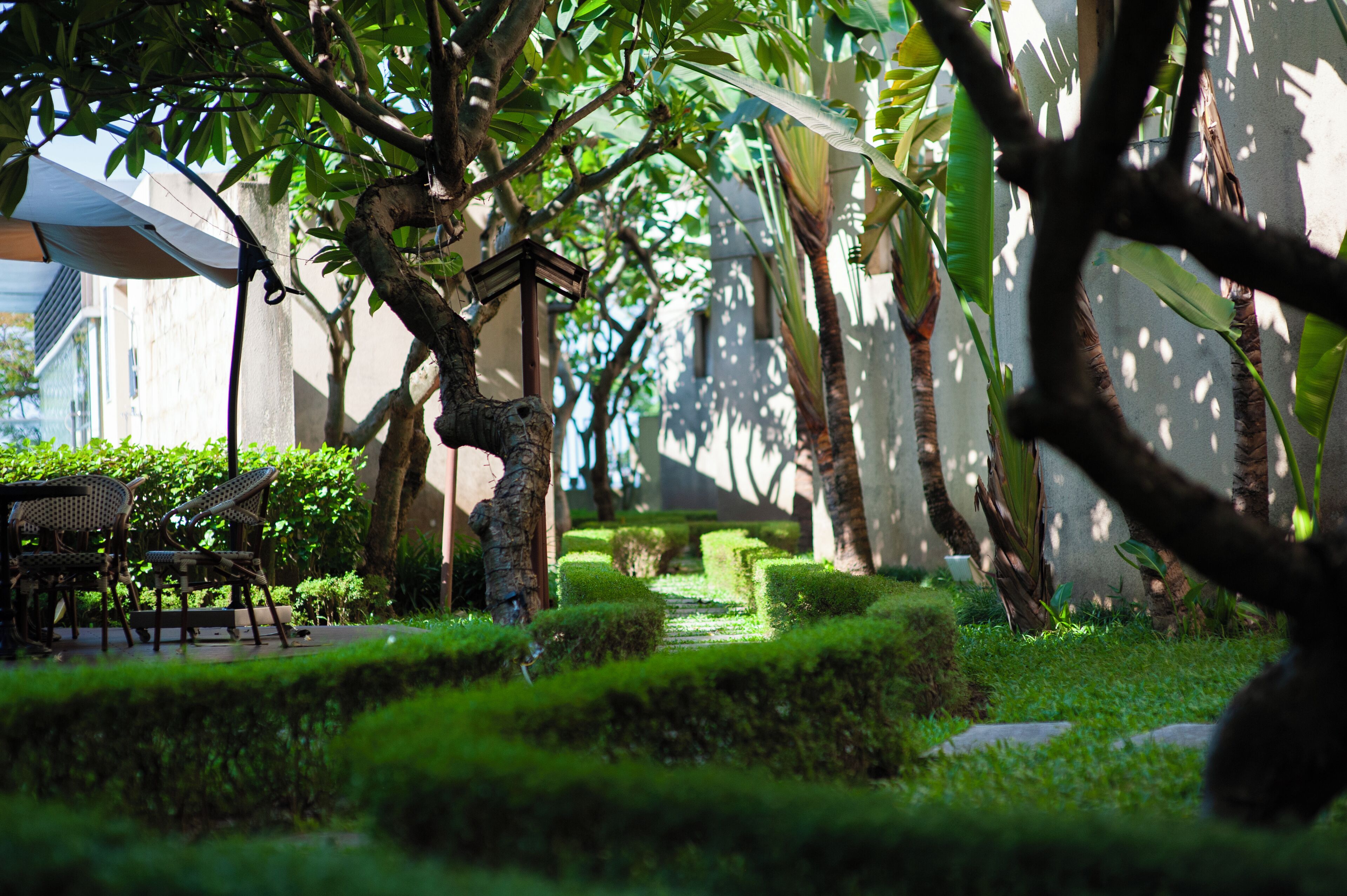 A garden with neatly trimmed hedges, a table with chairs, and a statue.