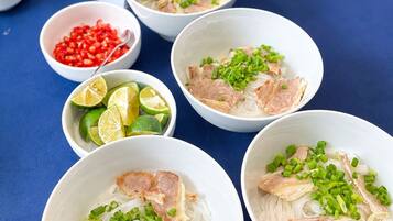 A table with bowls of noodle soup garnished with green onions and slices of meat, accompanied by small bowls of lime and chili peppers.
