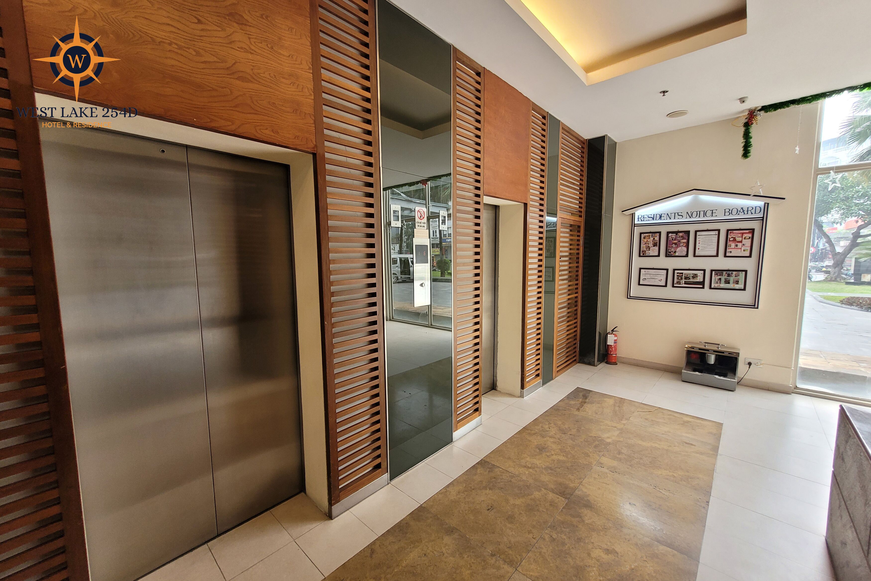 A hotel lobby with a modern design, featuring a reception desk, a residents notice board, and a fire extinguisher.