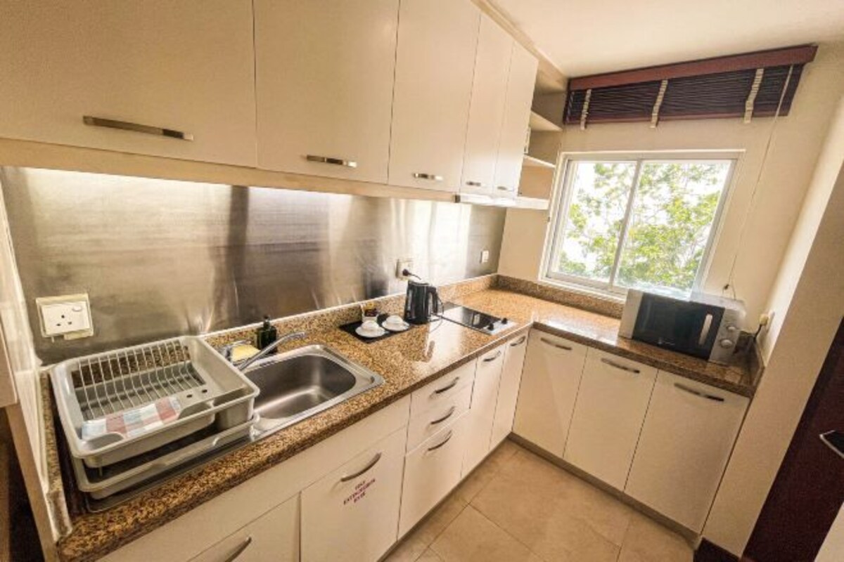A compact kitchen with stainless steel appliances, a dish rack, and a window providing natural light.