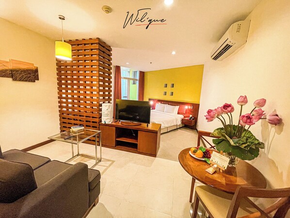 A hotel room with a bed, TV, wooden partition, seating area, and a dining table with flowers.