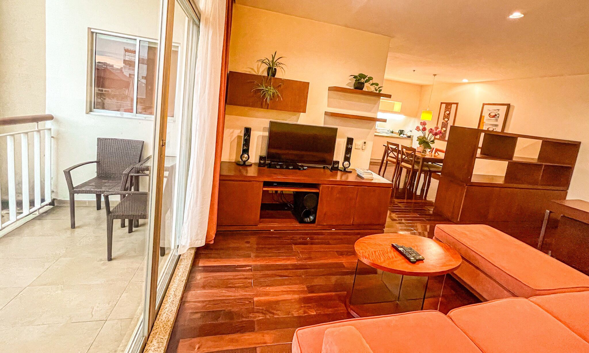 A modern living room with a TV, speakers, and a sofa. There is a dining area with chairs and a table.