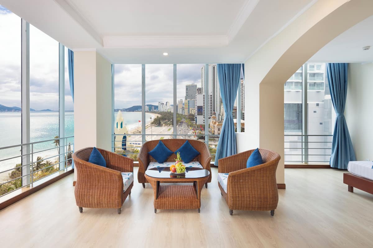 Ein Hotelzimmer mit Balkon, Korbmöbeln, einem Bett und Blick auf Stadt und Meer.
