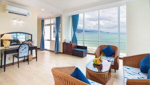 A modern room with a desk, wicker chairs, a small table with fruit, and a large window offering a view of the sea. - Nha Trang Lodge Hotel (Nha Trang)