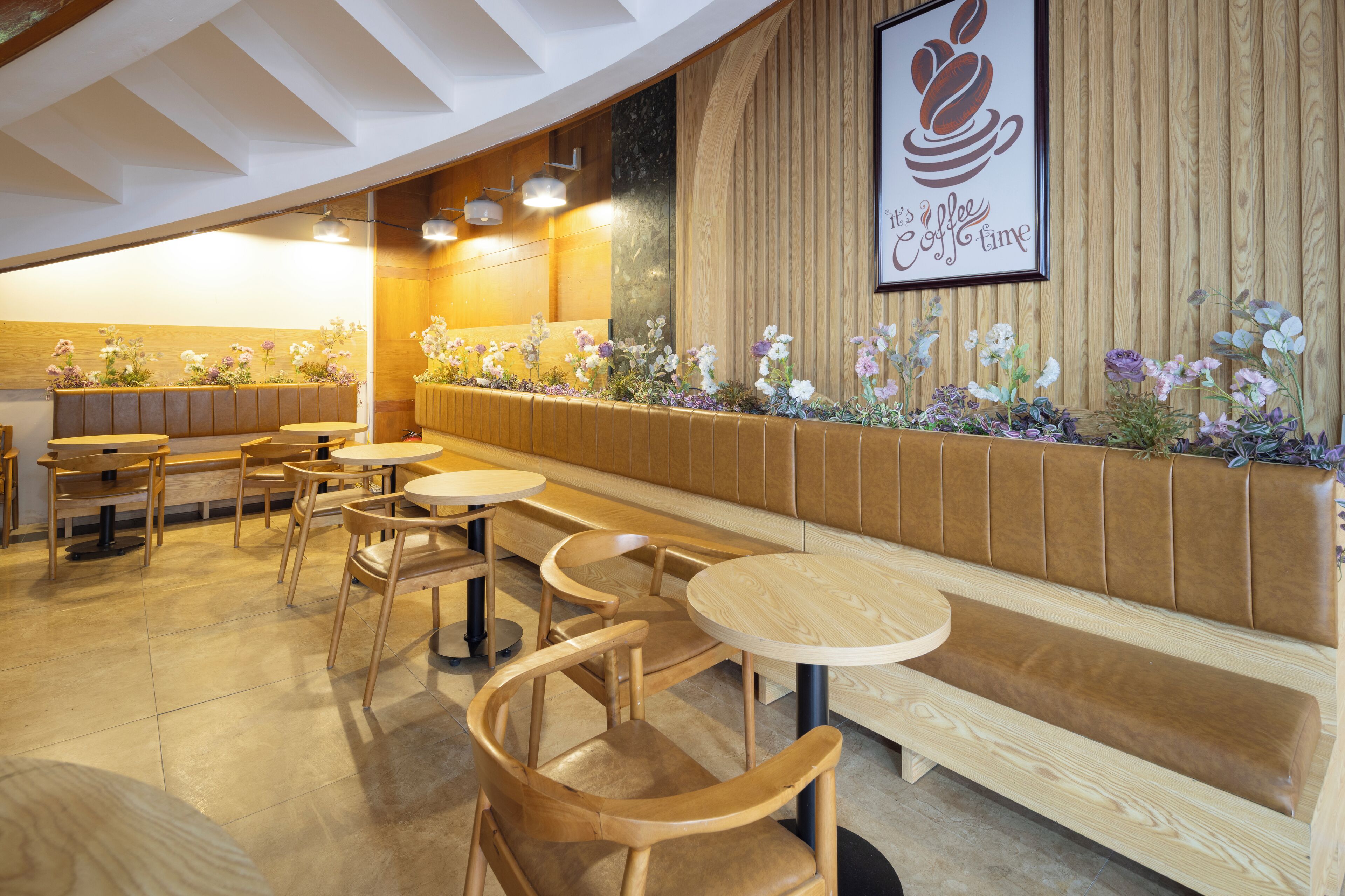 A restaurant interior with wooden furniture, a long bench, and a wall decorated with flowers and a coffee-themed artwork.