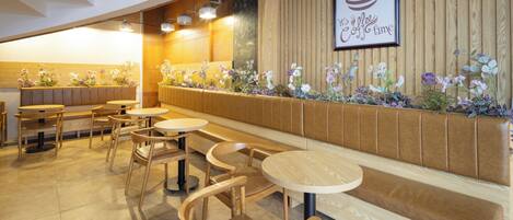 A restaurant interior with wooden furniture, a long bench, and a wall decorated with flowers and a coffee-themed artwork.