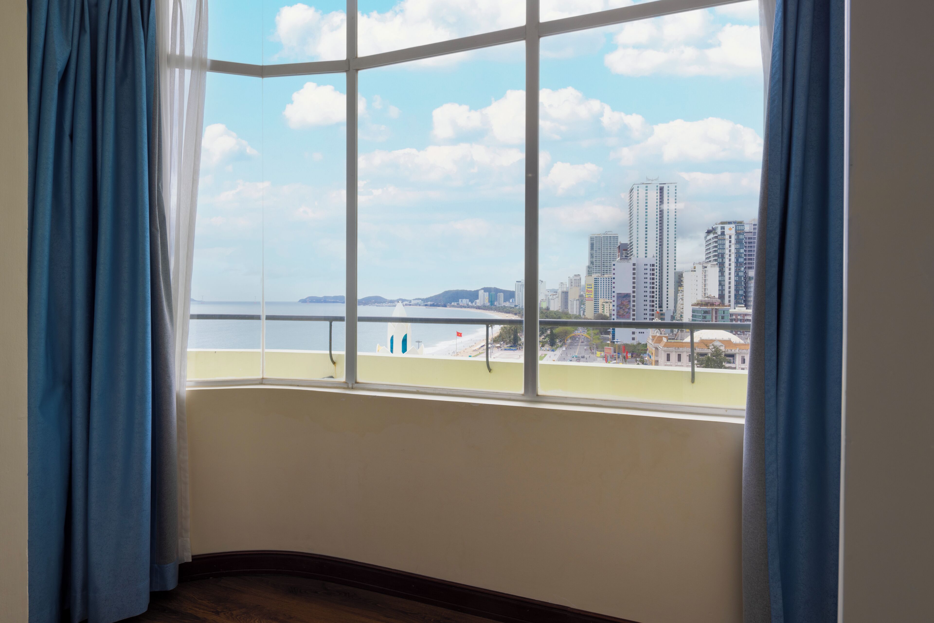 A room with a large window overlooking a beach and cityscape.