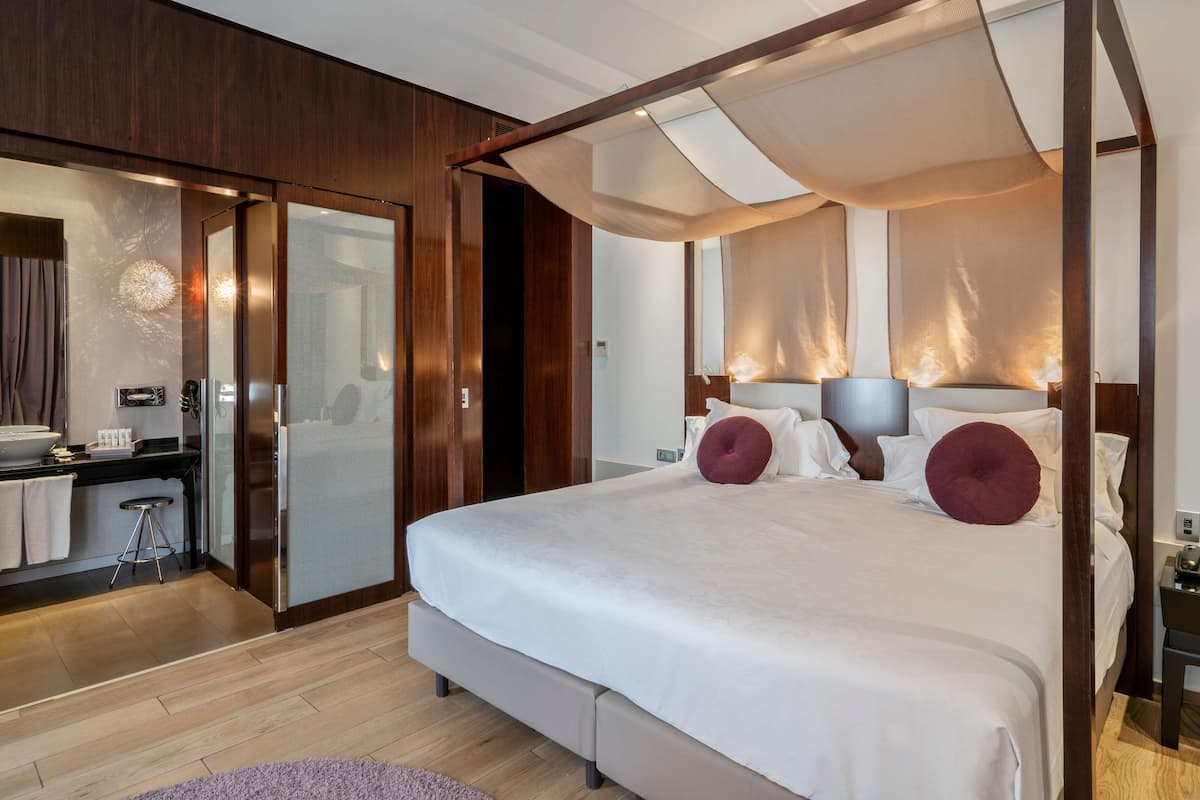 A modern bedroom with a canopy bed, a walk-in closet, and a bathroom with a large mirror.