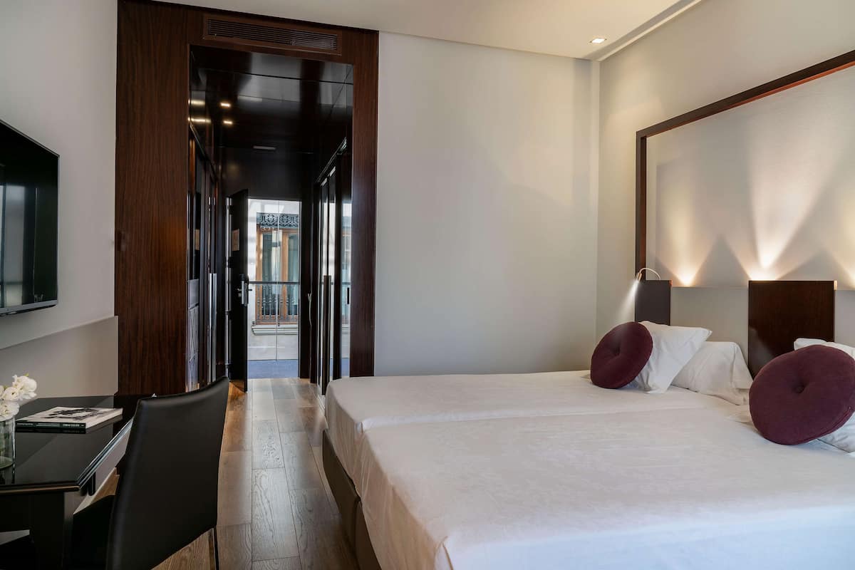 A hotel room with a large bed, a desk with a chair, and a television on the wall.