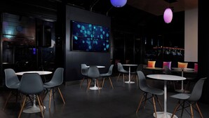 Un interior moderno con mesas y sillas redondas, una gran pantalla digital e iluminación ambiental.