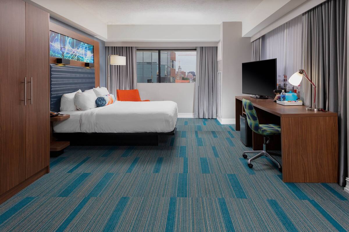 A hotel room with a bed, a desk, a television, and a city view.
