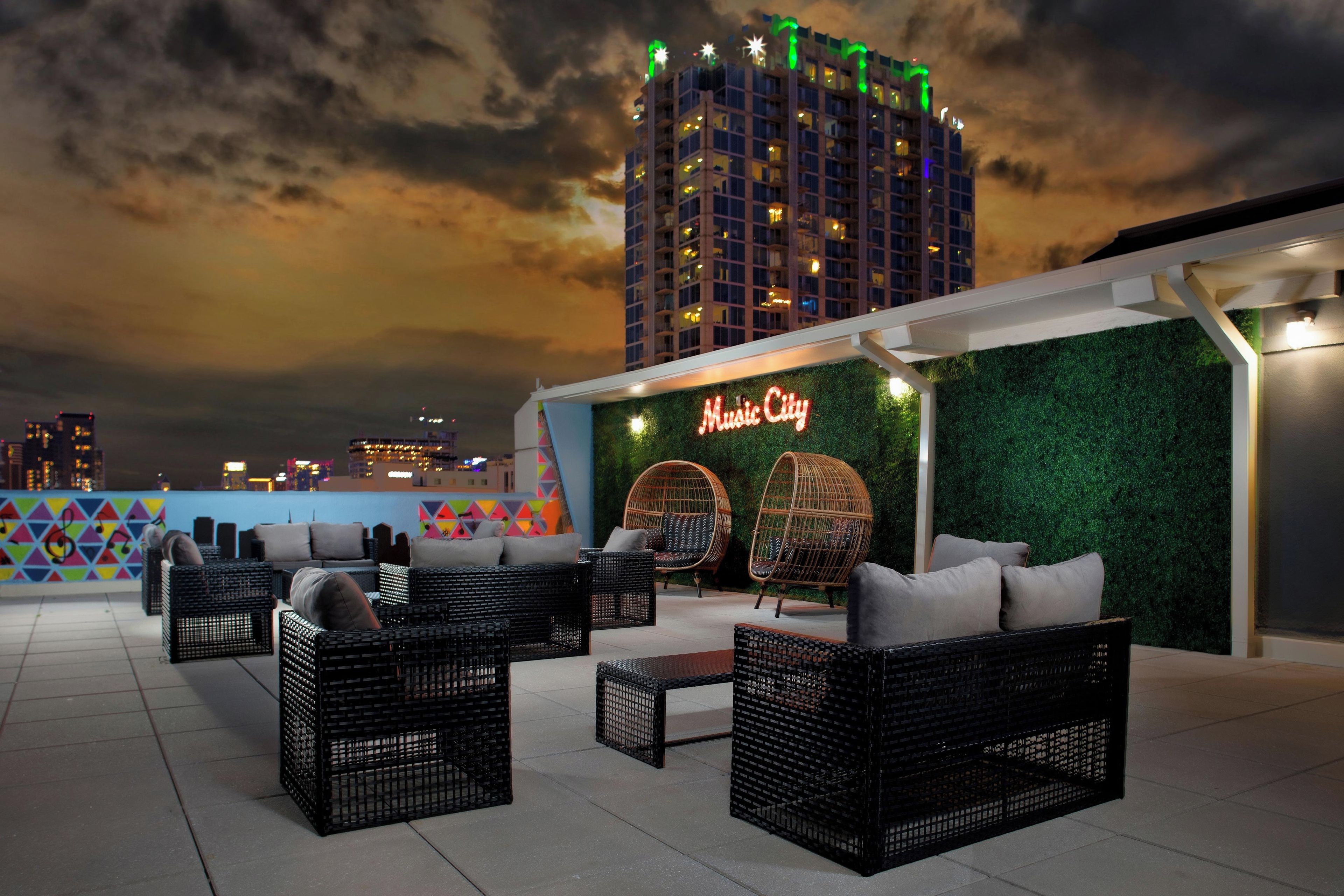 An outdoor seating area with wicker furniture and a green wall with a neon sign.