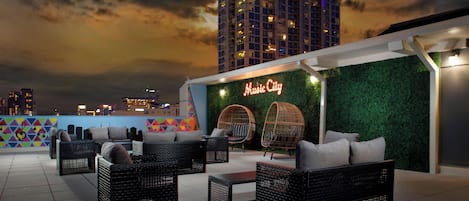 An outdoor seating area with wicker furniture and a green wall with a neon sign.