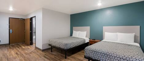 A room with two beds, a wooden floor, a teal accent wall, and a door.